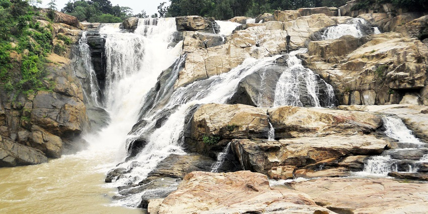A picture of a waterfall with water cascading down a cliff to create a pond near the Ormanjhi Water Park