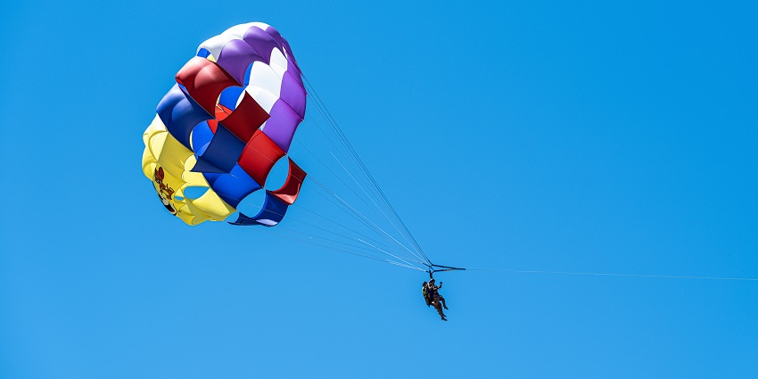 A breathtaking view of a colourful parachute in the sky with a man enjoying the sport.