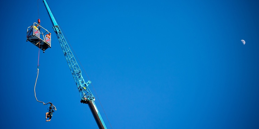 A man bungee jumping in Pokhara against a cloudy sky, with the cord stretched out.