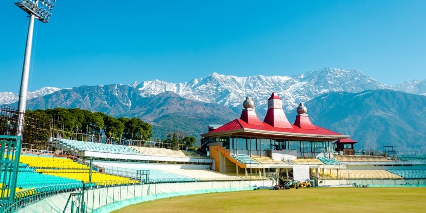 Image of Dharamshala cricket ground surrounded by lush green mountains under clear blue sky