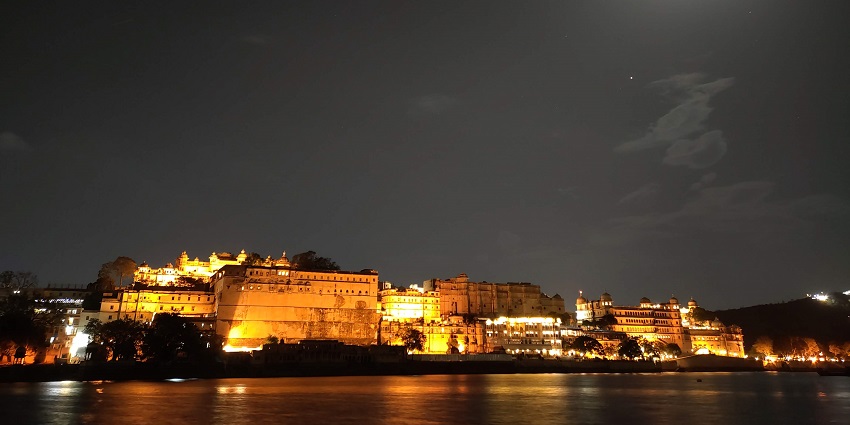 Ambrai Ghat at night in Udaipur, with illuminated buildings and a lively atmosphere