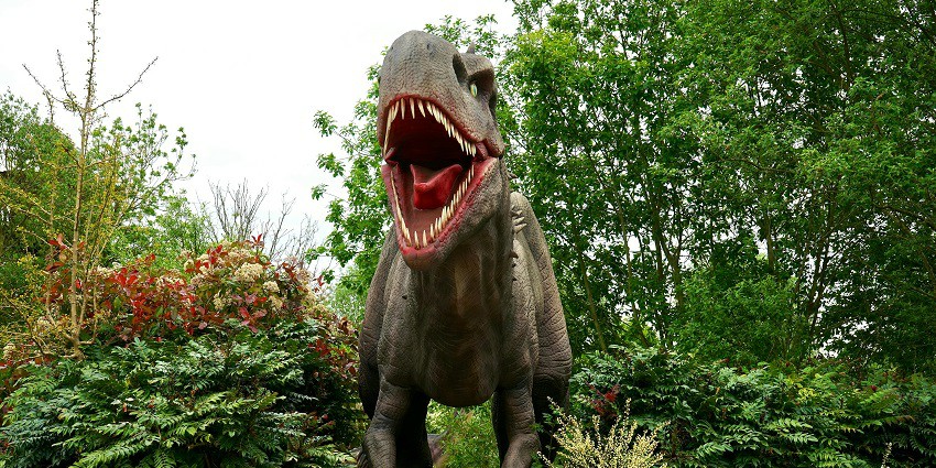 Image of a life-sized dinosaur sculpture amid lush greenery displayed in a park.