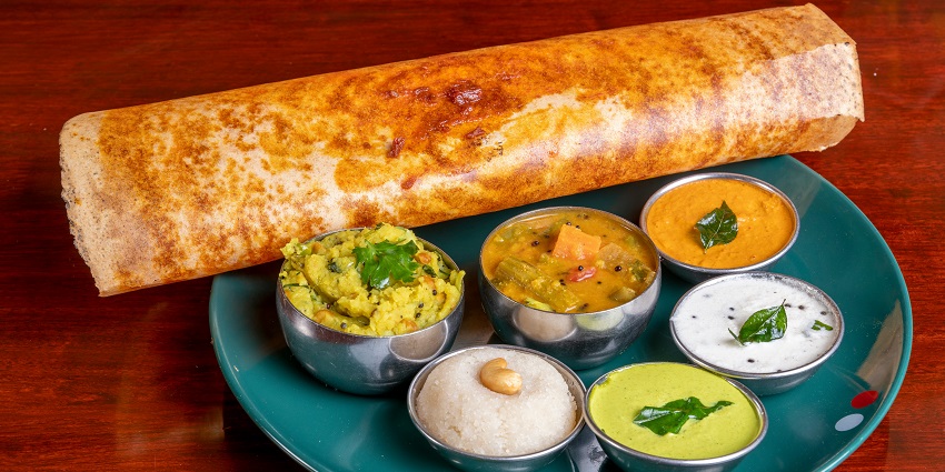 A glimpse of a crispy dosa served with aloo sabji, sambar and a variety of chutneys.