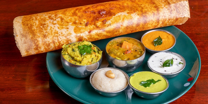 A view of a tempting dosa served on a plate with sambhar and other delicious dips.