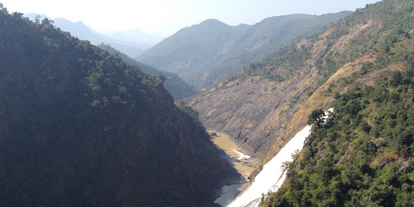 Waterfall partially shrouded in mist flowing down rocky terrain surrounded by greenery.
