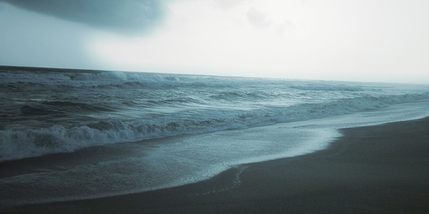 Serene view of waves crashing the sandy shores of the beach under a cloudy sky