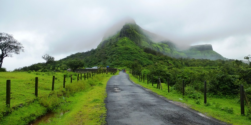 A picture of a road leading to a scenic trekking trail in Maharashtra, under a cover of clouds
