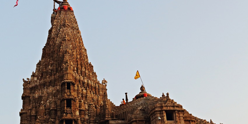 The towering spire of Dwarkadhish Temple, adorned with vibrant flags, stands tall at dusk.