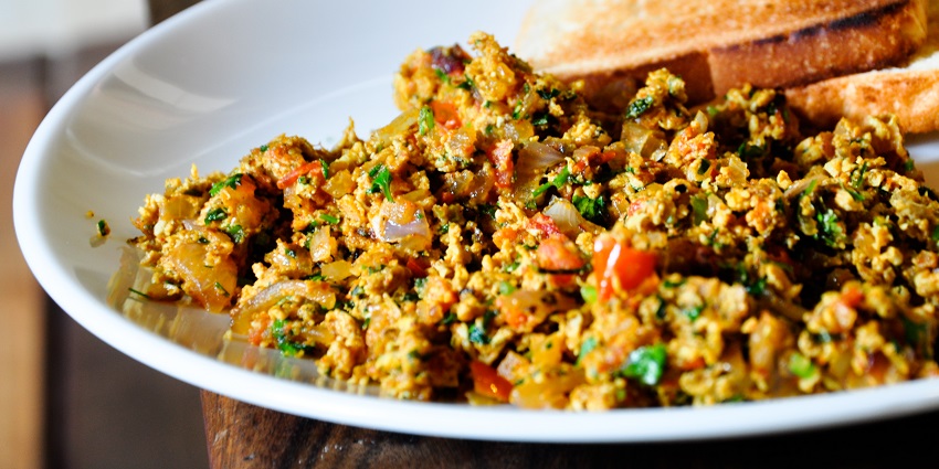 A glimpse of egg fried with veggies mint leaves sprinkled served with two slices of bread.