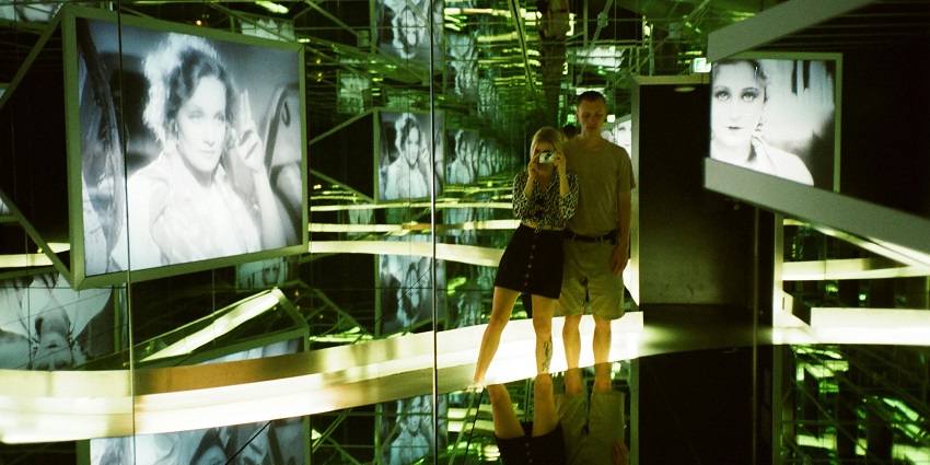 The beautiful painting behind a man and woman in the mirror gallery of the museum.