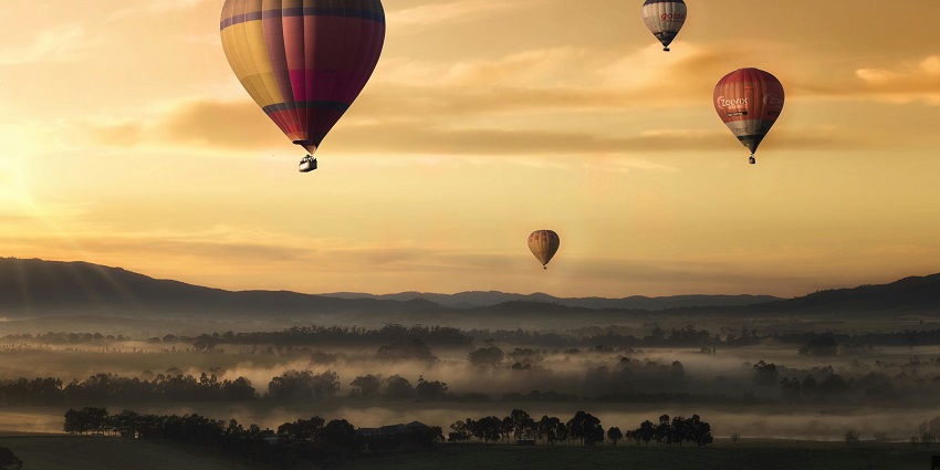 A view of a colourful hot air balloon ascending against a clear blue sky.