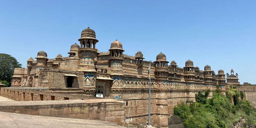An image of the majestic Gwalior Fort standing atop a hill against a clear blue sky.