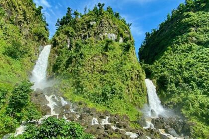 Image of twin waterfalls cascading through lush green rocks under clear blue sky