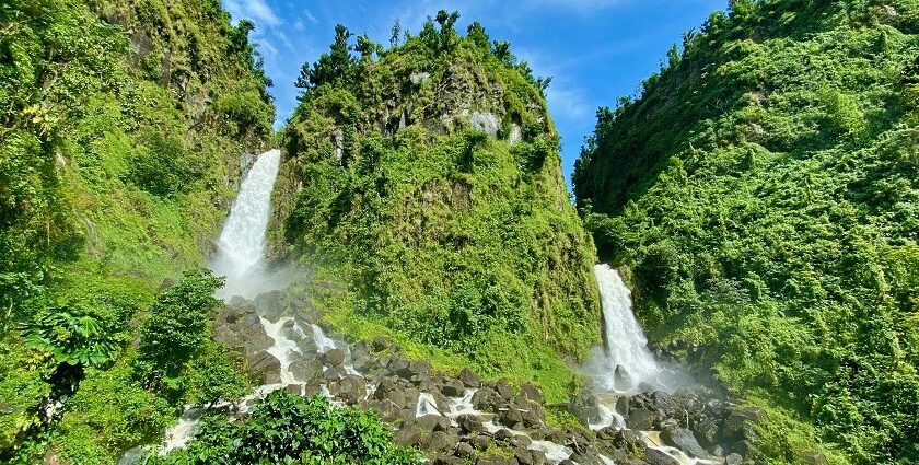 Image of twin waterfalls cascading through lush green rocks under clear blue sky