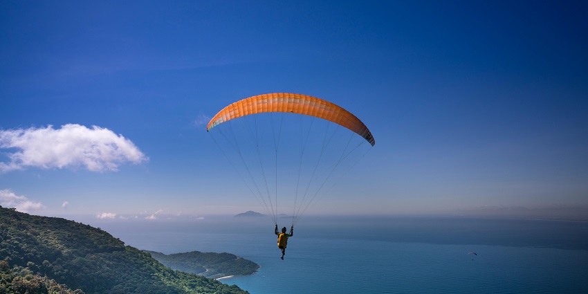 An image of a person paragliding in Mcleodgani and view of clear waters behind.