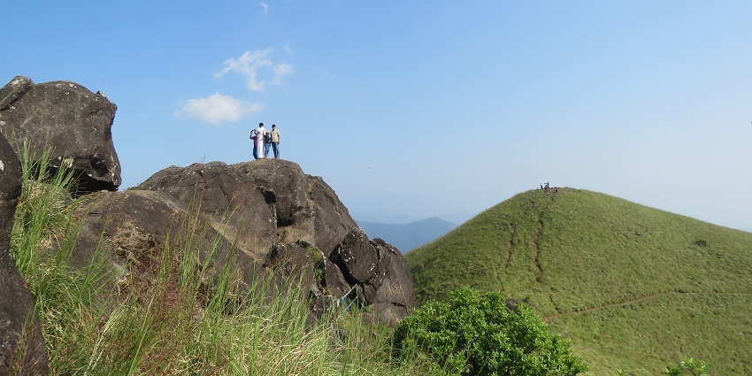 Two tourists standing on a large rock amidst the lush landscaped of the trekking trails
