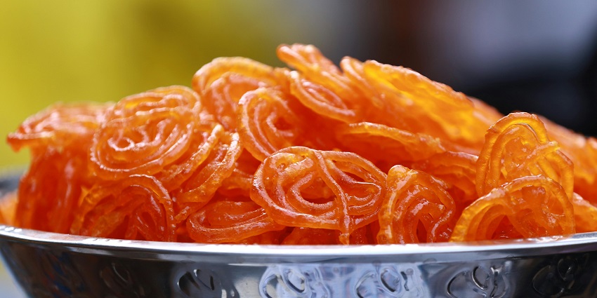 Delicious, juicy, and sweet Jalebi in bright orange colour served on a silver platter.