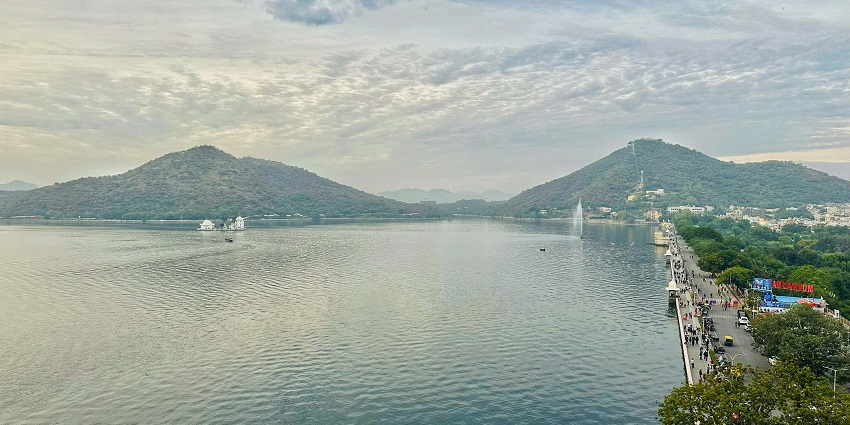 Crystal-clear blue waters of Fateh Sagar Lake, offering a serene view from the sidewalk.