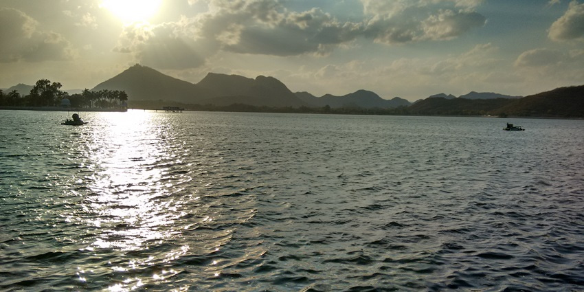 A peaceful view of Fateh Sagar Lake in Udaipur, framed by serene hills and vibrant greenery.