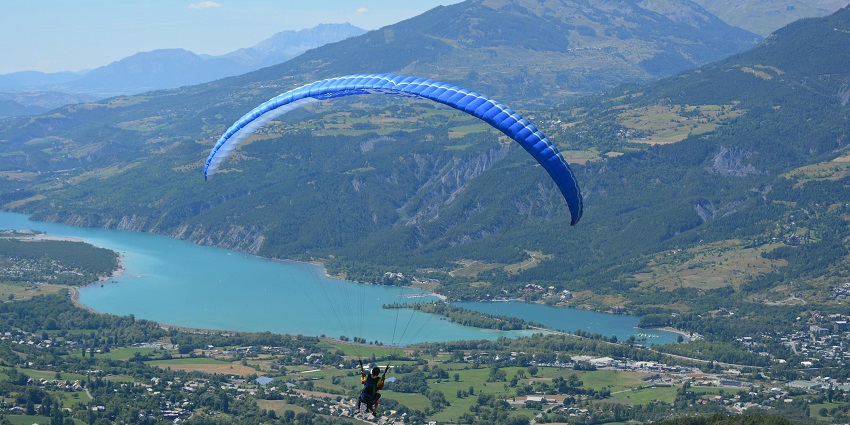 A view of a person swinging high up in the air above the shimmering lakes and lush peaks.