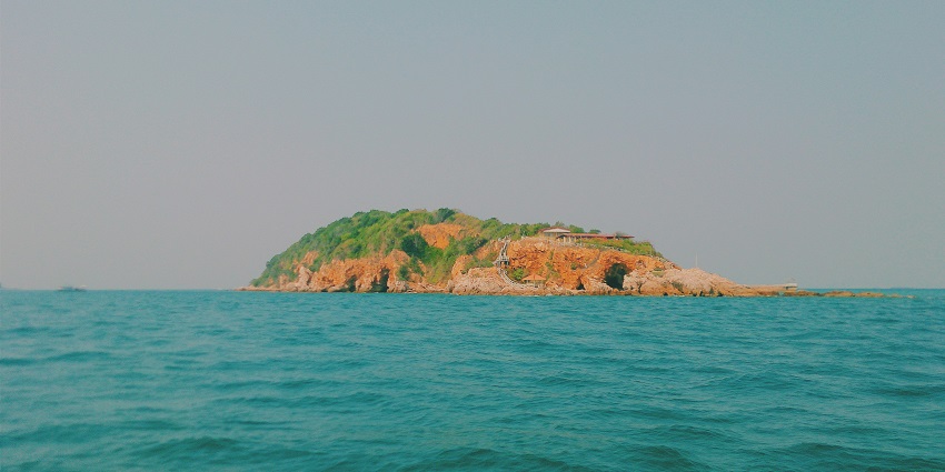 An image of Koh Larn beach, Thailand, with rocks on the shore and boats sailing.