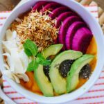 A tempting view of a bowl served with sliced fruits such as avocado and dragon fruit.