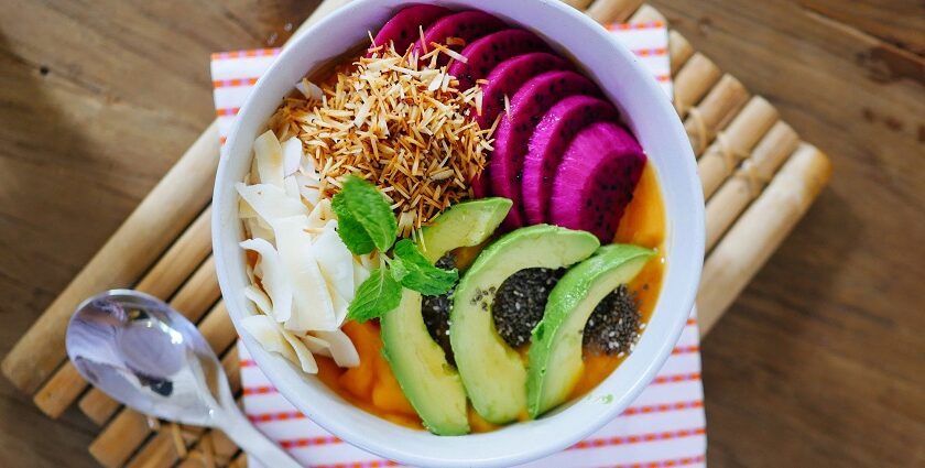 A tempting view of a bowl served with sliced fruits such as avocado and dragon fruit.