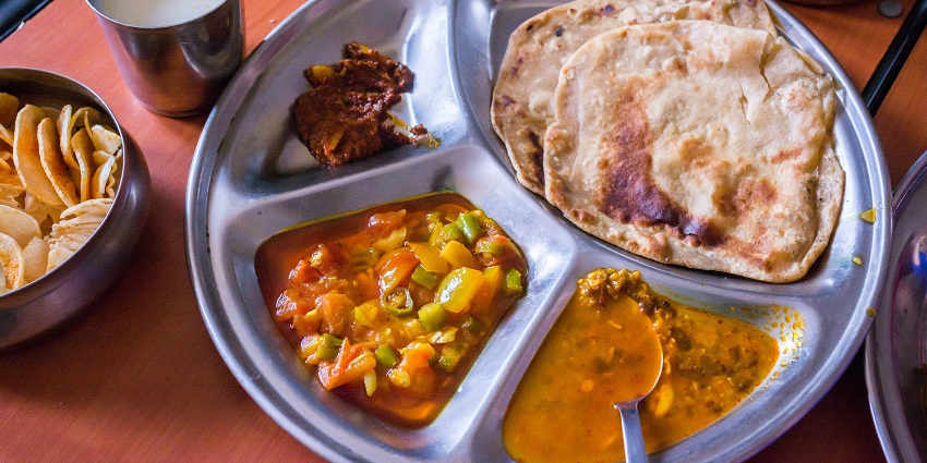 A round tray filled with a variety of colourful, cooked dishes ready to be served.