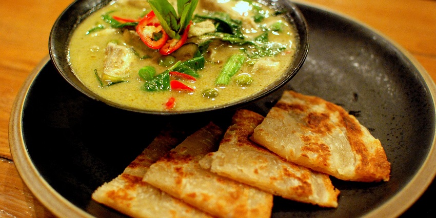 A delicious bowl of Thai green chicken curry served with warm, fluffy roti on the side