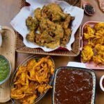 A glimpse of a variety of fritters being served with red and green chilli chutneys.