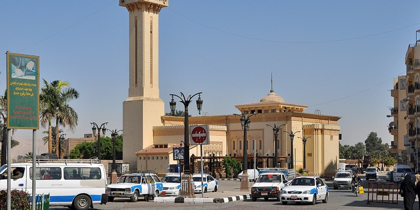 Modern mosque with a white façade and green dome, set against a clear sky.