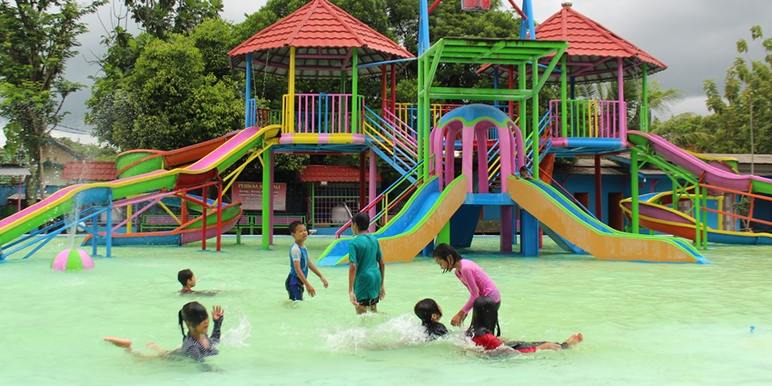 Image of kids playing in the water park surrounded by lush green trees during day time