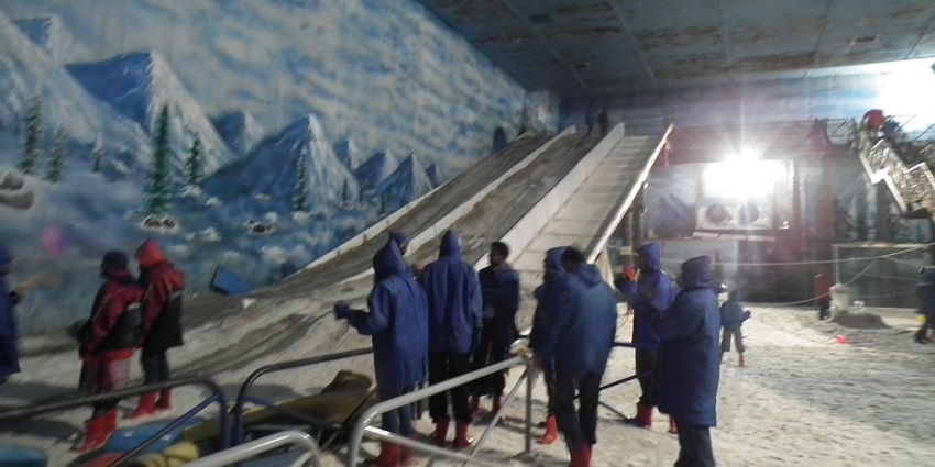 People enjoying snow activities in the snow park wearing snowsuits during the daytime.