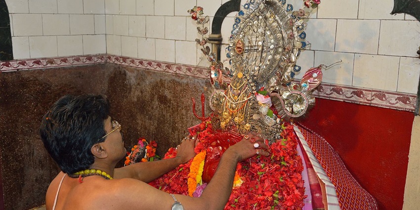 A picture of a priest decorating Goddess Chandi’s idol with garlands and flowers