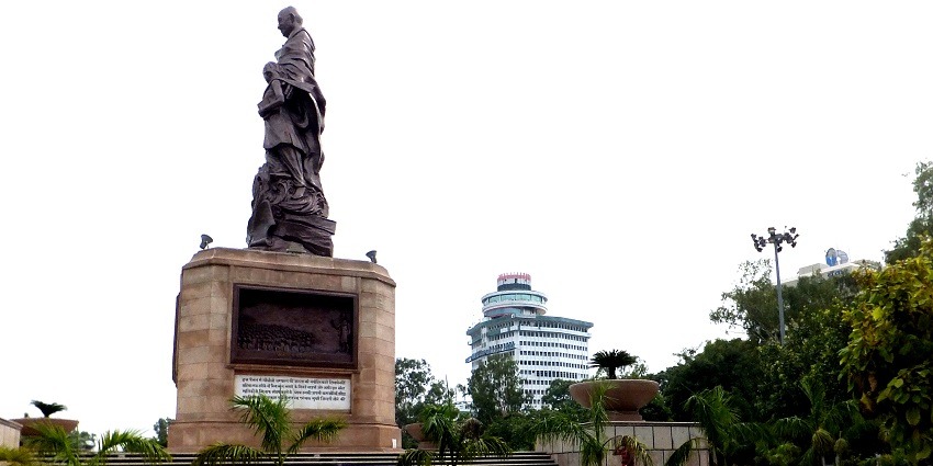 The statue of Mahatma Gandhi in Gandhi Maidan with a tall building in the background.