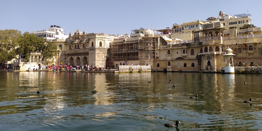 A historic ghat with shimmering reflections of havelis and temples on Lake Pichola at night.