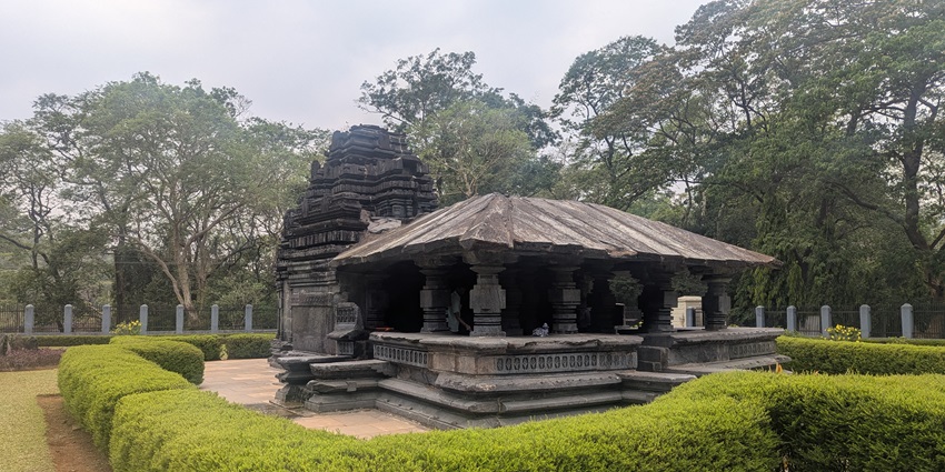 An image of a mahadev temple with intricate carvings, surrounded by lush forest.