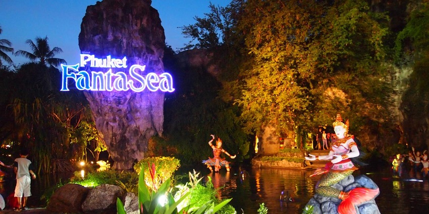 A giant rock amidst greenery and water with a vibrant display of lights and cultural statues