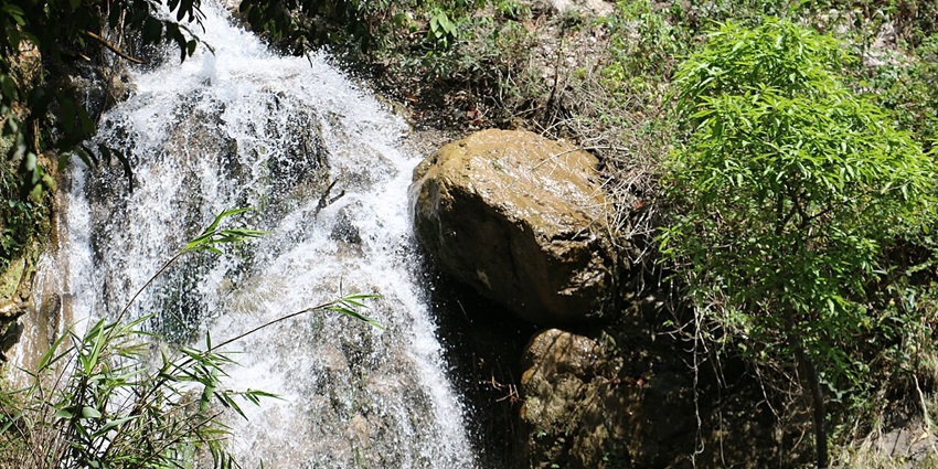 Seasonal waterfall near Giddalur flowing through rocky terrain, surrounded by lush greenery and forested hills.