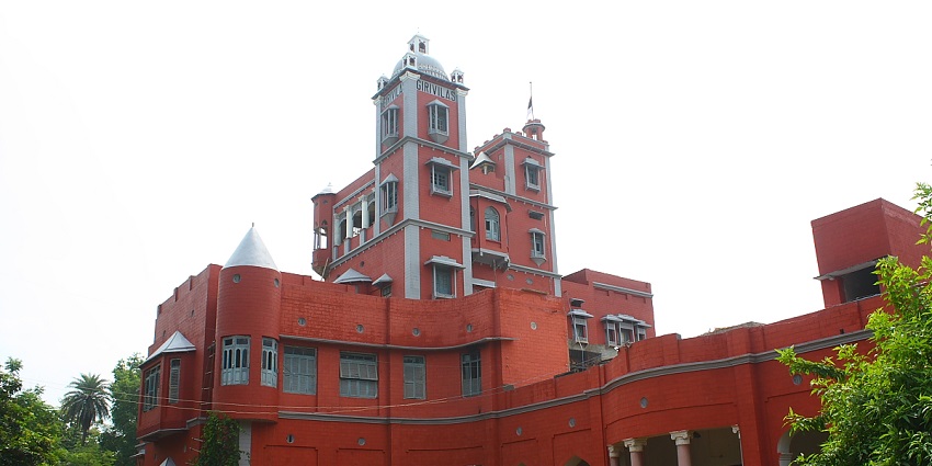 A picture of a renowned palace with red-brick walls and a garden area in front