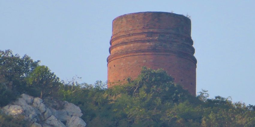 Distant view of the stupa, showing its prominent circular base amidst the scenic landscape of hills and valleys