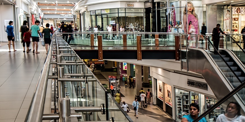 A view of the Modern Goa Shopping Centre with bright storefronts, escalators, and bustling shoppers.