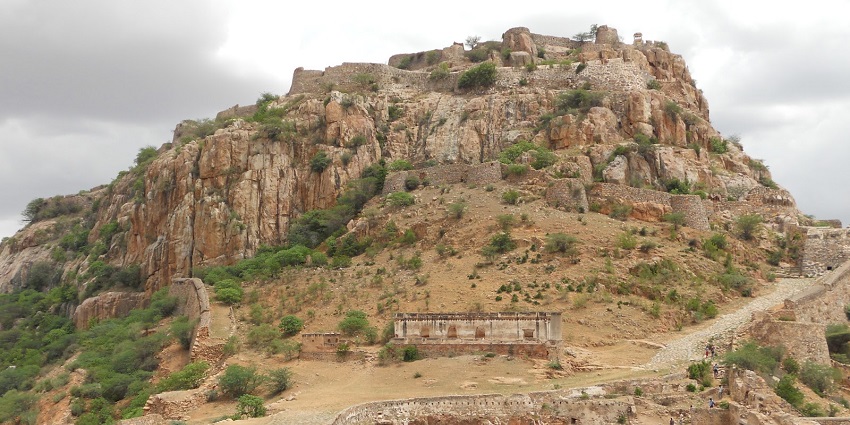 A distant picture of a fort situated on a hilltop with sandy rocks and several trees