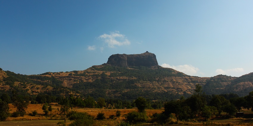 Looming above hills, this rugged plateau fort rises dramatically against the blue sky.