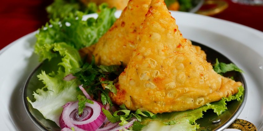 Image of two samosas served on a plate with veggies and onions