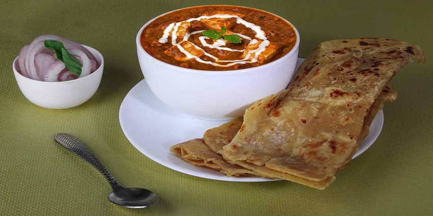 Indian meal combo with paneer butter masala, naan, rice, salad, and sliced onions.