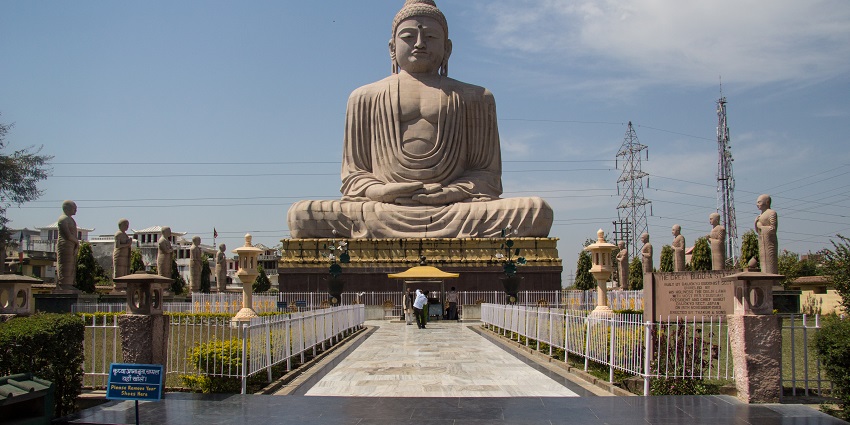 Towering stone sculpture of Buddha in a meditation pose with surrounding architectural elements