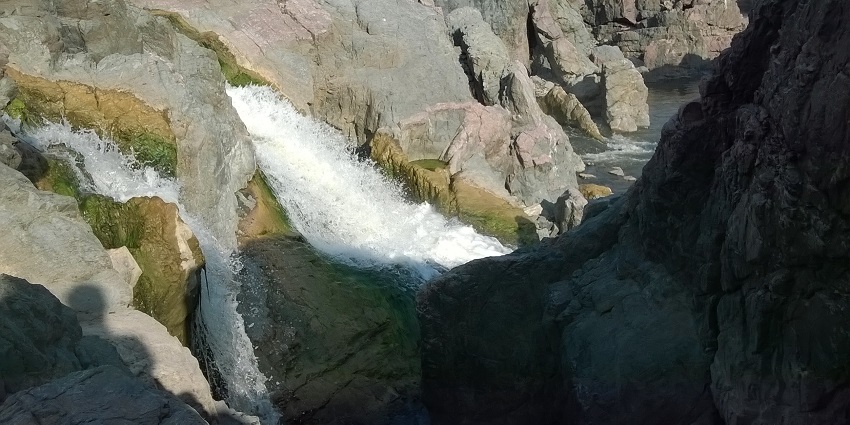 A picture of a waterfall cascading through big rocks and joining a river on its way further