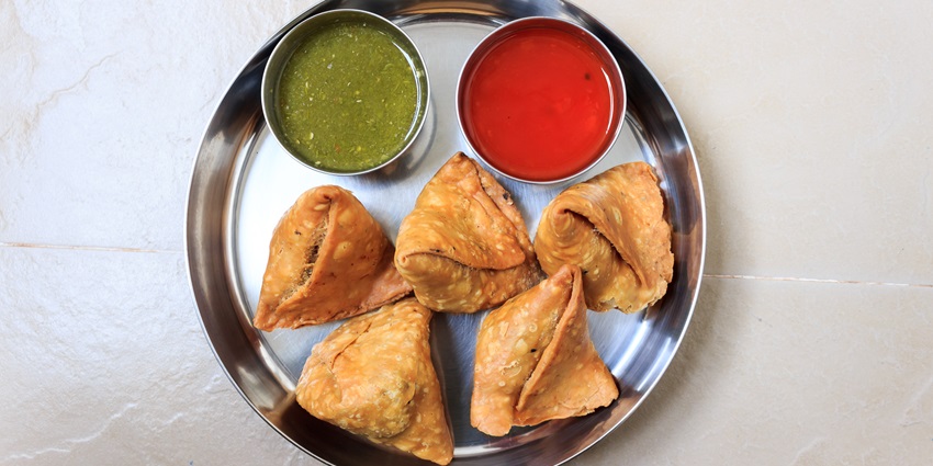Crispy samosas served with sweet red chutney and mint chutney, a flavorful combo