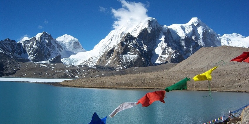 Majestic view of a Buddhist flag flapping over the lake with snow caped peaks in the background